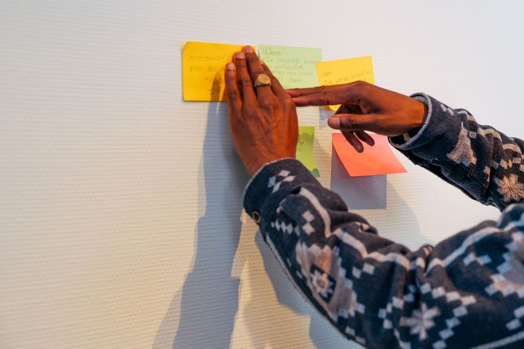 Twee handen plakken gekleurde post-its op een witte wand met begrippen als 'Wens' tijdens een Human Centric werksessie